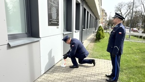 Policjant kładzie znicz przed tablicą