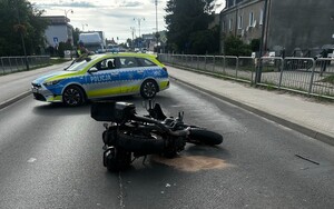 Rozbity motocykl leży na ulicy. Za nim stoi radiowóz