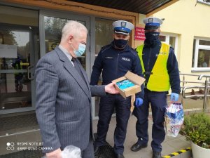 Dwóch umundurowanych policjantów wręcza maski dyrektorowi Domu Pomocy Społecznej w Młodzieszynie