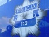 Zdjęcie przedstawia policyjną odznakę na niebieskim tle. Na odznace w kształcie gwiazdy zamieszczono napis POLICJA, a poniżej numer alarmowy 112