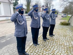 Czterech policjantów w umundurowaniu galowym salutuje przed pomnikiem