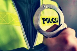 Policjant trzyma w ręku kajdanki.