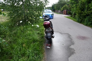 Na drodze asfaltowej stojący skuter po wypadku. W tle radiowóz.