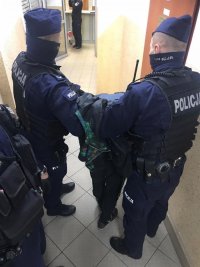 Na zdjęciu widzimy 2 umundurowanych policjantów którzy prowadzą zatrzymanego mężczyznę.