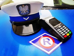 Terminal płatniczy na masce radiowozu wraz z czapką policjanta ruchu.