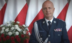 Na zdjęciu na tle flagi Komendant Główny Policji gen. insp. dr Jarosław Szymczyk, po lewej stronie biało czerwone kwiaty.
