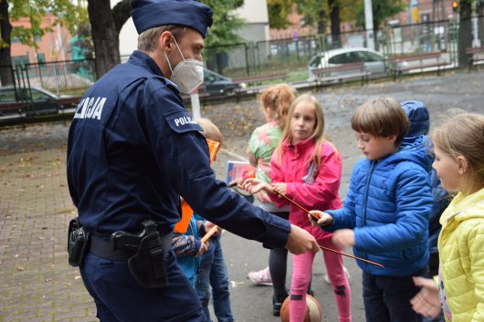 Policjant rozdający odblaski dzieciom, które stoją przed nim.