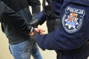 zdjęcie przedstawia rękę policjanta umundurowanego który zakłada kajdanki na ręce przestępcy trzymane z tyłu