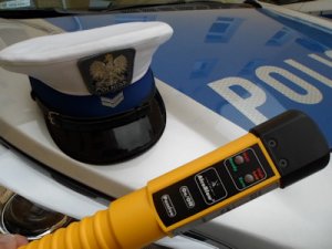 na zdjęciu widoczne jest urządzenie do pomiaru ilości alkoholu w wydychanym powietrzu, czapka policjanta ruchu drogowego oraz przód radiowozu